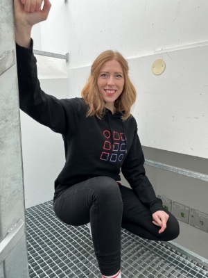 Zeige Details für FI Iconic unisex  Weibliches Model trägt schwarzen Hoody mit Kapuze und buntes Logo auf der Vorderseite