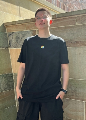 Zeige Details für FI Rainbow  Model vor Steinwand mit schwarzem T-Shirt mit Finanz Informatik Logo in Regenbodenfarben